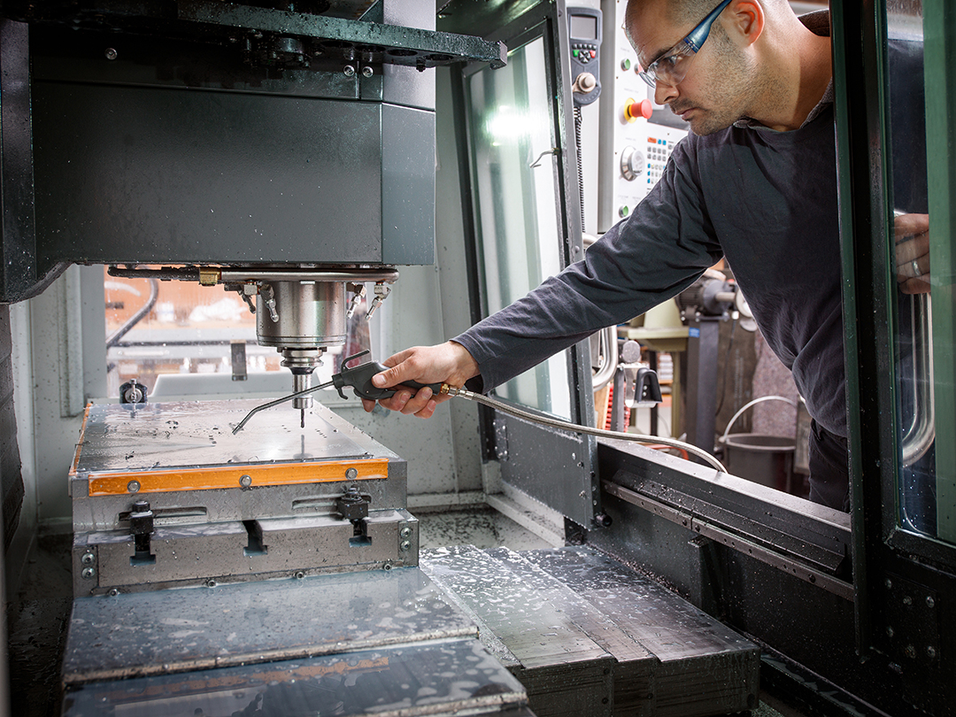 knife factory worker spraying liquid onto machiner