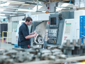 male worker inspecting parts on cnc lathe in engine