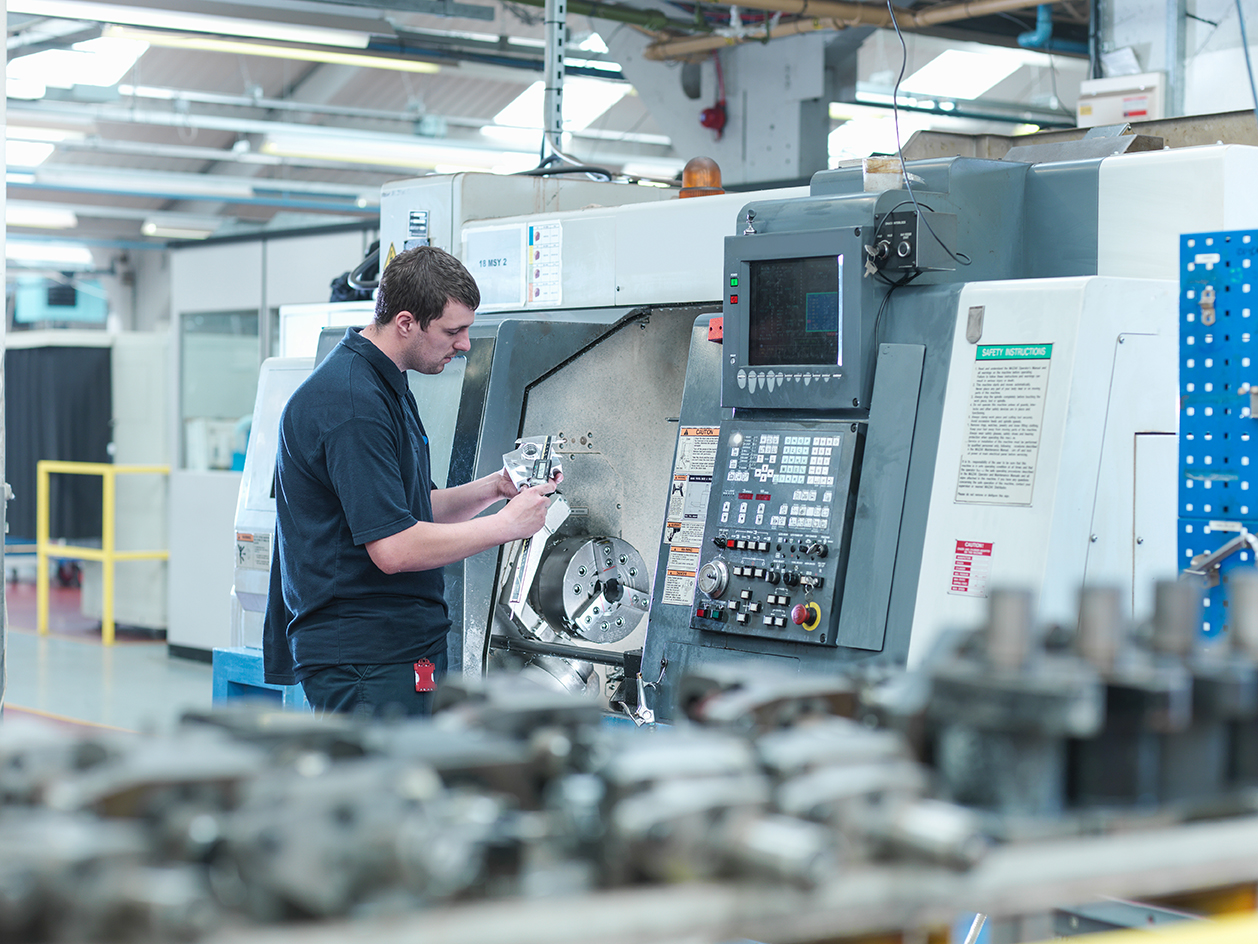 male worker inspecting parts on cnc lathe in engine